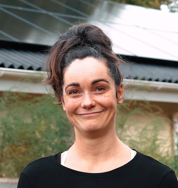 Smilende kvinde foran et hus med solpaneler på taget.